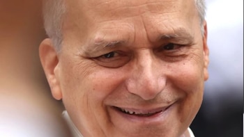 Primer plano del rostro de un hombre mayor sonriendo, con piel arrugada, cabello blanco ralo y ojos oscuros expresando calidez