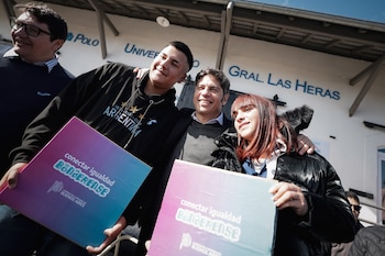Tres personas sonríen mientras sostienen cajas con el logo 'Conectar Igualdad Bonaerense' frente a un edificio con la inscripción 'Polo Universitario Gral. Las Heras'