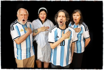 Cuatro personas, dos hombres y dos mujeres, con camisetas de Argentina. Tres tienen la mano derecha en el pecho y las bocas abiertas. Fondo negro