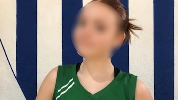 Joven con rostro difuminado, camiseta deportiva verde con dos rayas blancas, posa frente a fondo de franjas verticales azules y blancas
