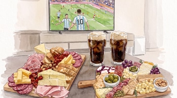 Televisión con partido de fútbol y jugadores de Argentina, dos tablas con quesos, fiambres, panes y frutos secos, y dos vasos de fernet con espuma.