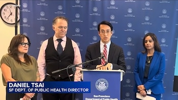 Daniel Tsai, diretor de saúde pública de São Francisco, fala em um palco com um microfone, junto com três pessoas durante uma coletiva de imprensa.