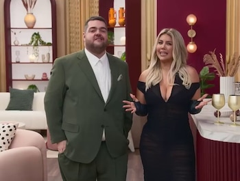 Wanda Nara, con vestido negro escotado, y Darío Barassi, con traje verde, de pie en un set de televisión moderno con estantes y muebles