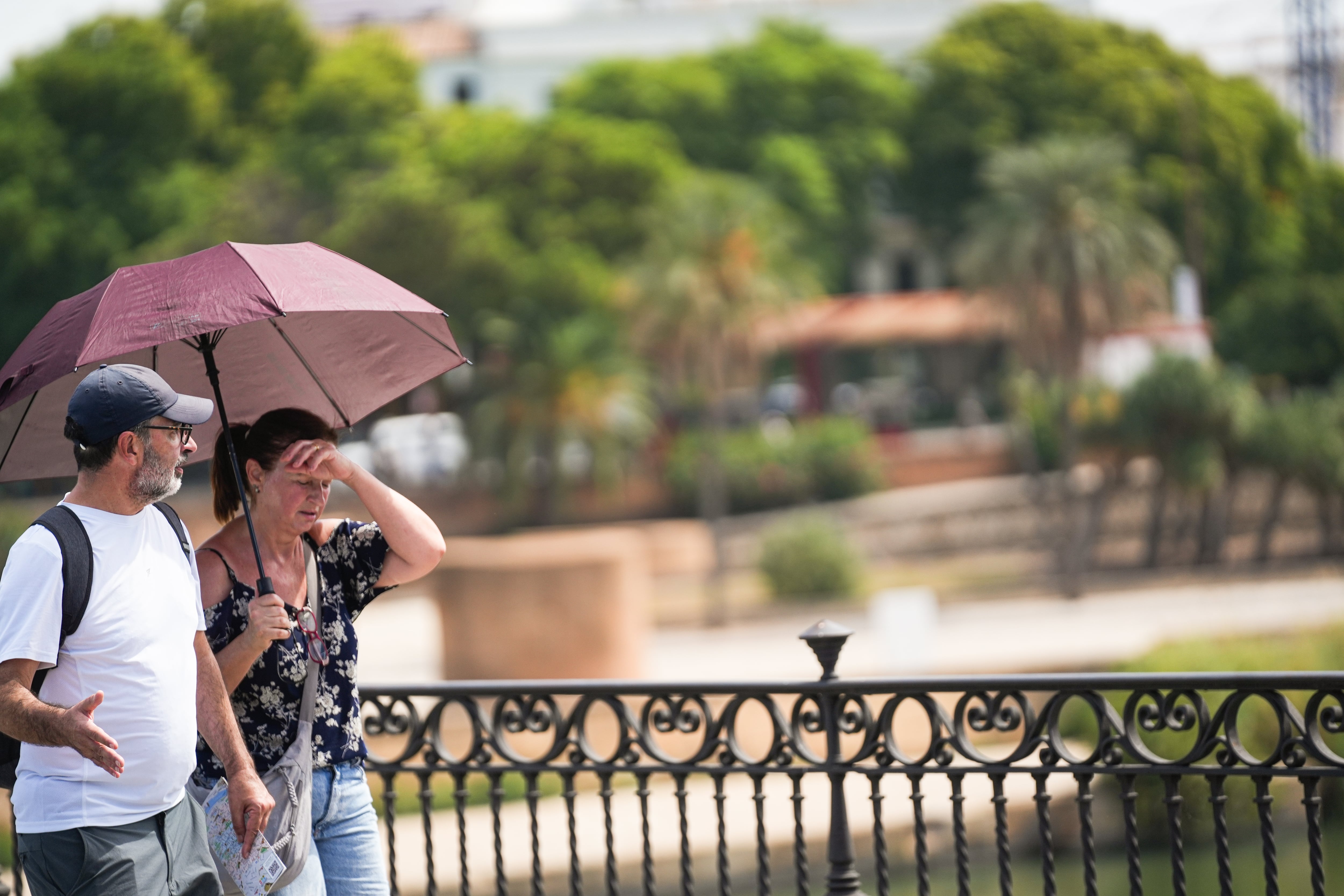 Dos personas con sombrilla y ropa veraniega durante una jornada de intenso calor en Sevilla. (María José López/Europa Press)