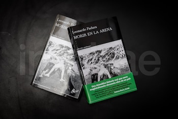 Primer plano de dos libros idénticos, "Morir en la arena" de Leonardo Padura, sobre una superficie oscura. Las portadas muestran una foto en blanco y negro de personas en la playa