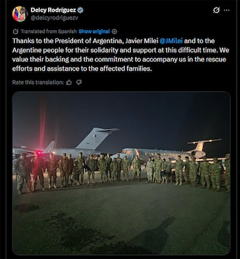 Un grupo de más de veinte personas con uniformes militares y varios perros posa frente a dos aviones en una pista de aterrizaje oscura