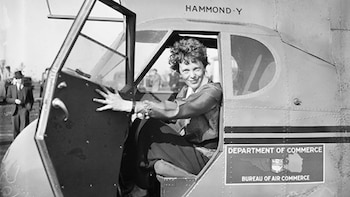 Uma mulher sorri na cabine aberta de um avião. É lido