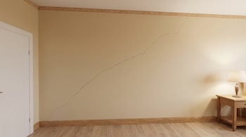 Pared beige con una larga grieta diagonal, piso de madera, marco de puerta blanca y mesita de noche con lámpara.