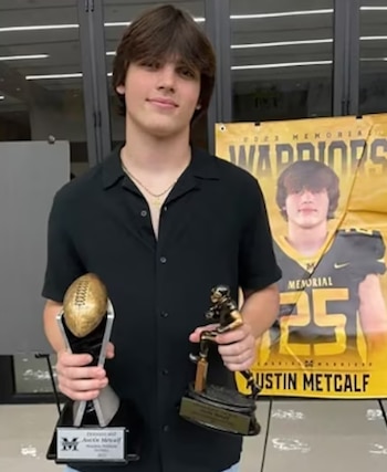 Un joven con camisa negra sostiene dos trofeos dorados frente a un cartel amarillo con su nombre y su fotografía