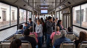 Interior de un autobús con hombres y mujeres sentados y de pie sujetándose de los pasamanos metálicos.