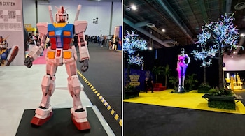 Figura a tamaño real de robot Gundam blanco, azul, rojo y amarillo en exposición. Fondo con personas y códigos QR.