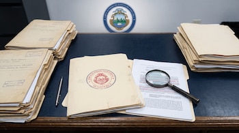 Pilas de expedientes legales, una carpeta con el sello de la Corte Suprema de Justicia de Costa Rica, un bolígrafo y una lupa sobre un documento.