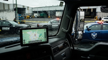 Pantalla GPS en cabina de camión muestra Cuautitlán Izcalli. Patrullas SSEM con escudo de águila y cinta amarilla en predio industrial exterior.