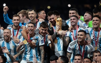 Messi abrazado a la Copa del Mundo, rodeado de sus compañeros en Qatar. La Selección iniciará la defensa del título (Foto EFE)