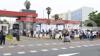 Vista exterior de la entrada principal de la Universidad Nacional Mayor de San Marcos con una multitud de personas, personal de seguridad y un vehículo blanco