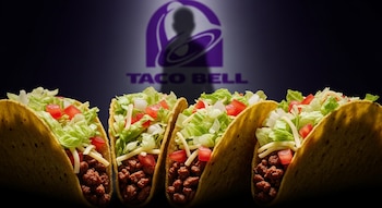 Cuatro tacos abiertos con carne, lechuga, tomate y queso sobre fondo oscuro; en segundo plano, el logo de Taco Bell desenfocado con una sombra.
