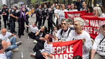 Protesta en la calle con activistas sentados y de pie, sosteniendo pancartas rojas y usando camisetas con el mensaje 'Fund People Not Bombs', con presencia policial y detenciones