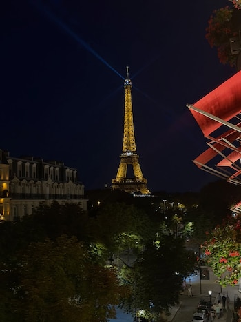 La Torre Eiffel iluminada, edificios, árboles, estructuras de color rojo a la derecha y una calle con vehículos y personas de noche