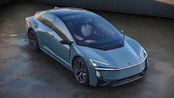 Vista aérea de un automóvil Toyota Corolla Concept de color gris azulado, con luces LED frontales, techo oscuro y rines negros, estacionado sobre asfalto mojado