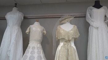 Cuatro maniquíes exhiben vestidos de novia blancos y crema, con detalles de encaje y volantes, en una sala con paredes grises