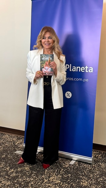 Mujer rubia de pie, saco blanco, pantalón negro, sostiene libro titulado "El Poder de Ser Tú". Fondo azul con texto "Planeta" y logo