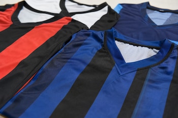 Tres camisetas de fútbol con franjas rojas, azules y negras se encuentran extendidas sobre una superficie.