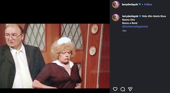 Un hombre con traje y una mujer rubia con cofia blanca y vestido oscuro, ambos con expresiones serias, aparecen en un escenario teatral con fondo de madera