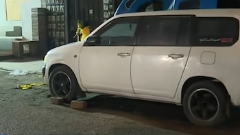 Un automóvil familiar de color blanco estacionado de noche sobre el asfalto, con ladrillos colocados debajo de una rueda delantera