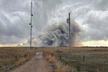 Densa columna de humo negro y gris sobre un campo seco bajo cielo nublado, con torre de comunicaciones y poste eléctrico en primer plano