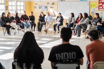 Decenas de personas sentadas en pupitres individuales dentro de un aula con computadoras portátiles y cuadernos
