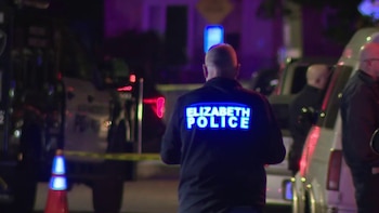 Un policía de espaldas con la inscripción Elizabeth Police en su abrigo frente a patrullas, conos y cinta policial en la noche