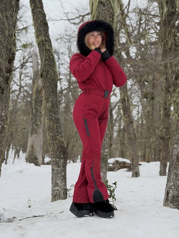 Una mujer viste un traje térmico rojo con capucha de piel negra sobre la nieve entre árboles