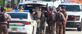Varios agentes de policía con equipo táctico permanecen junto a patrullas de la oficina del alguacil con luces encendidas