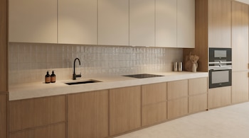 Cocina moderna con gabinetes de madera clara y crema, encimera clara, fregadero negro, placa de inducción y hornos empotrados, vista frontal.