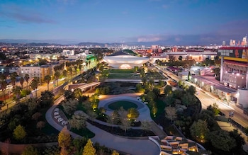 Vista aérea de noche del Lucas Museum of Narrative Art, un edificio blanco ovalado rodeado de un parque con senderos iluminados y una ciudad al fondo