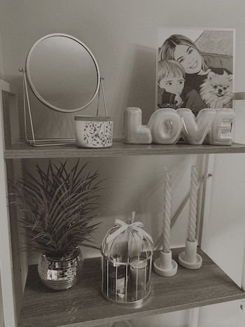 Estantería con espejo circular, bote decorado, letras "LOVE", ilustración enmarcada de mujer, niño y perro, planta en maceta y dos velas