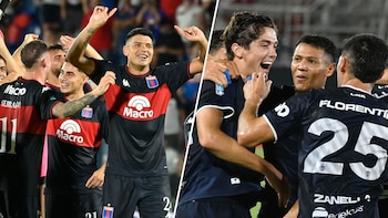Dos grupos de jugadores de fútbol celebrando en un estadio, vestidos con uniformes diferentes, uno negro y rojo, y otro azul oscuro, mostrando alegría