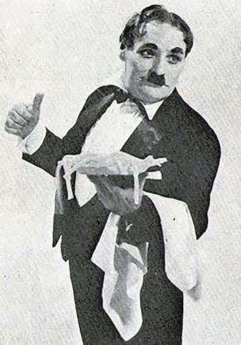 Tandarica en blanco y negro, con bigote, traje, camisa y pajarita. Levanta el pulgar y sostiene un paño. Fondo liso y claro