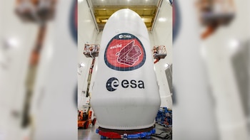 El carenado blanco de un cohete espacial con el logotipo de la misión Euclid y el de la ESA es trabajado por dos operarios en elevadores en un hangar