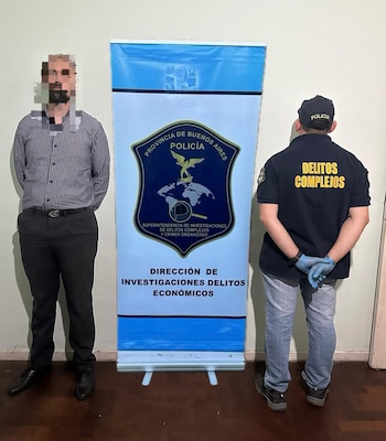 Un hombre con rostro borroso y un oficial de policía de espaldas con guantes azules posan frente a un banner azul y blanco de la Policía de Buenos Aires