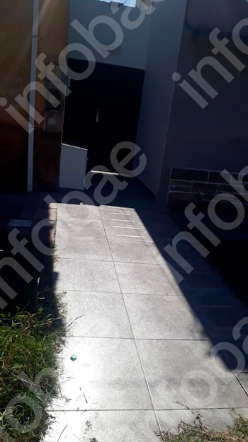 Un camino de concreto con baldosas, flanqueado por césped, lleva a la entrada de una edificación, con sombras proyectadas y luz solar