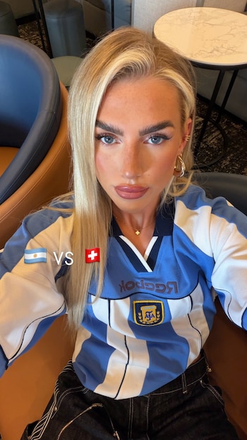 Mujer rubia con camiseta de fútbol de Argentina con logo Reebok y escudo, collar, aretes, y texto "VS" entre banderas de Argentina y Suiza