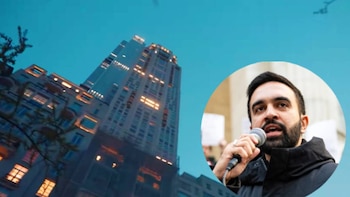 Un rascacielos iluminado en Nueva York sirve de fondo para el retrato de Zohran Mamdani, hablando por micrófono