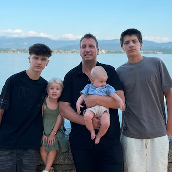 Un hombre, Maxi López, sostiene un bebé. A su lado, dos adolescentes y una niña posan. Detrás se ve un lago y montañas al fondo