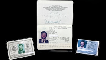 Un pasaporte de Estados Unidos abierto junto a dos tarjetas de identificación con fotografías de un hombre con barba y anteojos