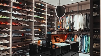Vestidor moderno con estantes llenos de zapatillas y ropa. Percheros con prendas. Una isla central con una caja de accesorios