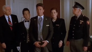 Cinco personas vestidas con uniformes de hotel y trajes formales permanecen de pie dentro de un vestíbulo frente a una puerta blanca