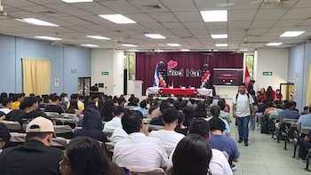 Auditorio con personas sentadas frente a un escenario decorado con el logotipo de Red Hat, globos, banderas y una pantalla