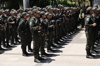 Un grupo de agentes uniformados con ropa verde oscura, gorras y fusiles se encuentra formado en filas en una plaza al aire libre