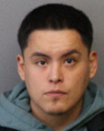 Fotografía frontal de un hombre joven con cabello oscuro y corto, rostro serio y sudadera, mirando directamente a la cámara. El fondo es liso y de color claro